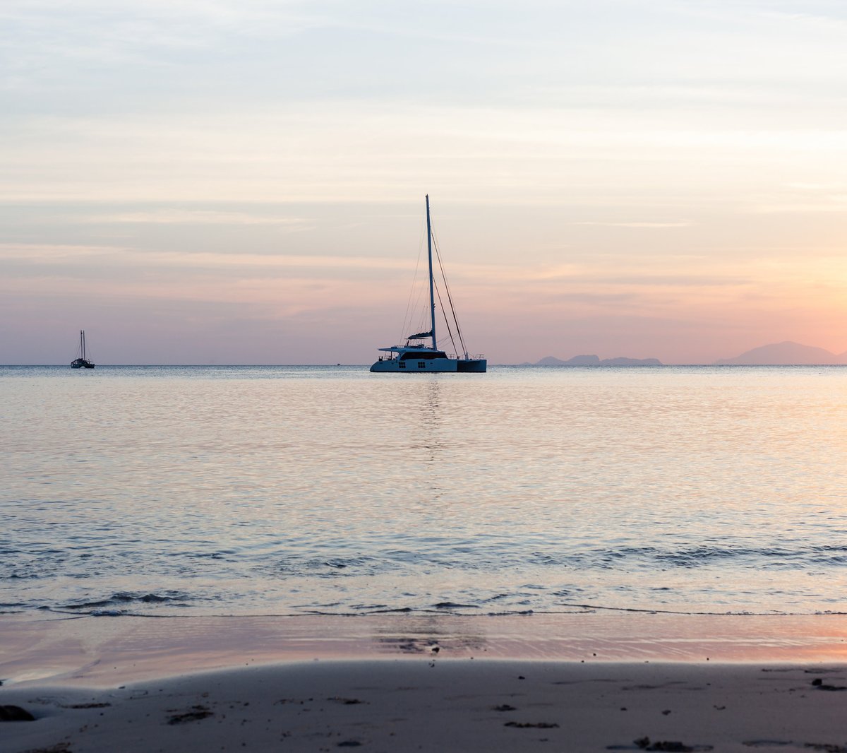 Luxury catamaran anchored at sunset over calm sea with golden light